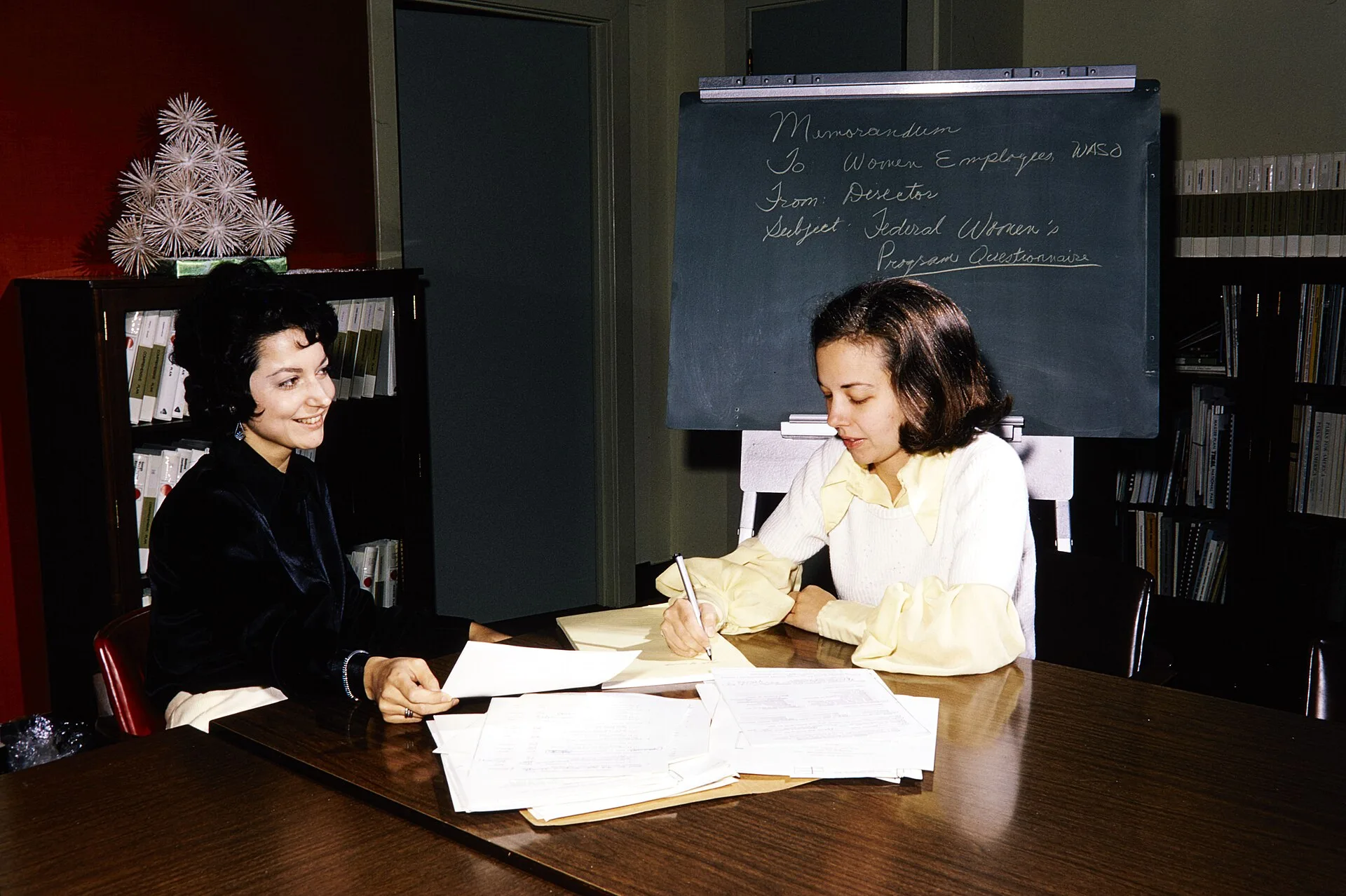 NPS employees looking through paperwork in the Womens Program in Washington Office. Keywords: nps staff; desk; NPS Personnel(NPS History Collection Themes); Women(NPS History Collection Themes); Communications(NPS History Collection Themes)