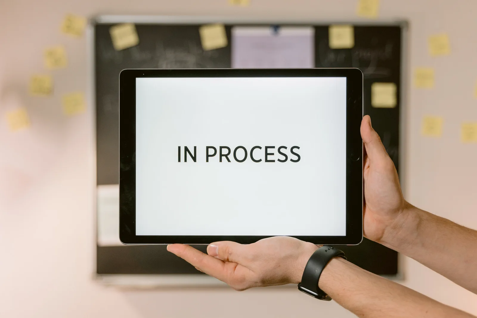 Close-up of hands holding a tablet displaying 'In Process' text, emphasizing workflow.