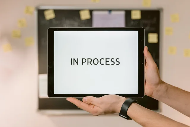 Close-up of hands holding a tablet displaying 'In Process' text, emphasizing workflow. What proposal software foundations mean for B2B vendor strategy